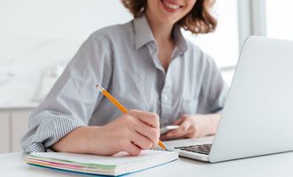 Ung jente smiler og tar notater for hånd og på datamaskin
