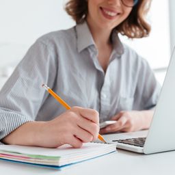 Young girl smiling taking notes by hand and on computer
