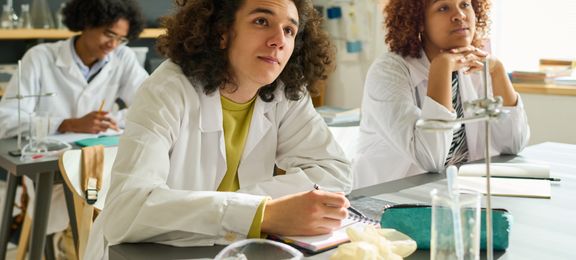 Happy teenage boy in labcoat looking at teacher of natural sciences