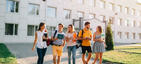 Fem studenter går rundt med bøker på campus på universitetet